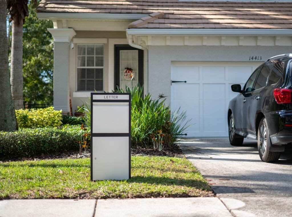 A Feliluke package delivery box stands on a driveway next to a residential home, offering secure parcel storage.