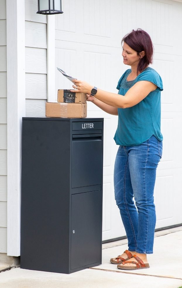 A woman is standing in front of the black Feliluke delivery locker, checking the mail. She places a package she just retrieved on top of the locker.