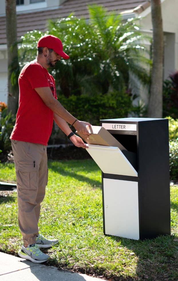 A deliveryman wearing a red uniform is depositing mail into the black and white Feliluke delivery locker on the porch of my house.