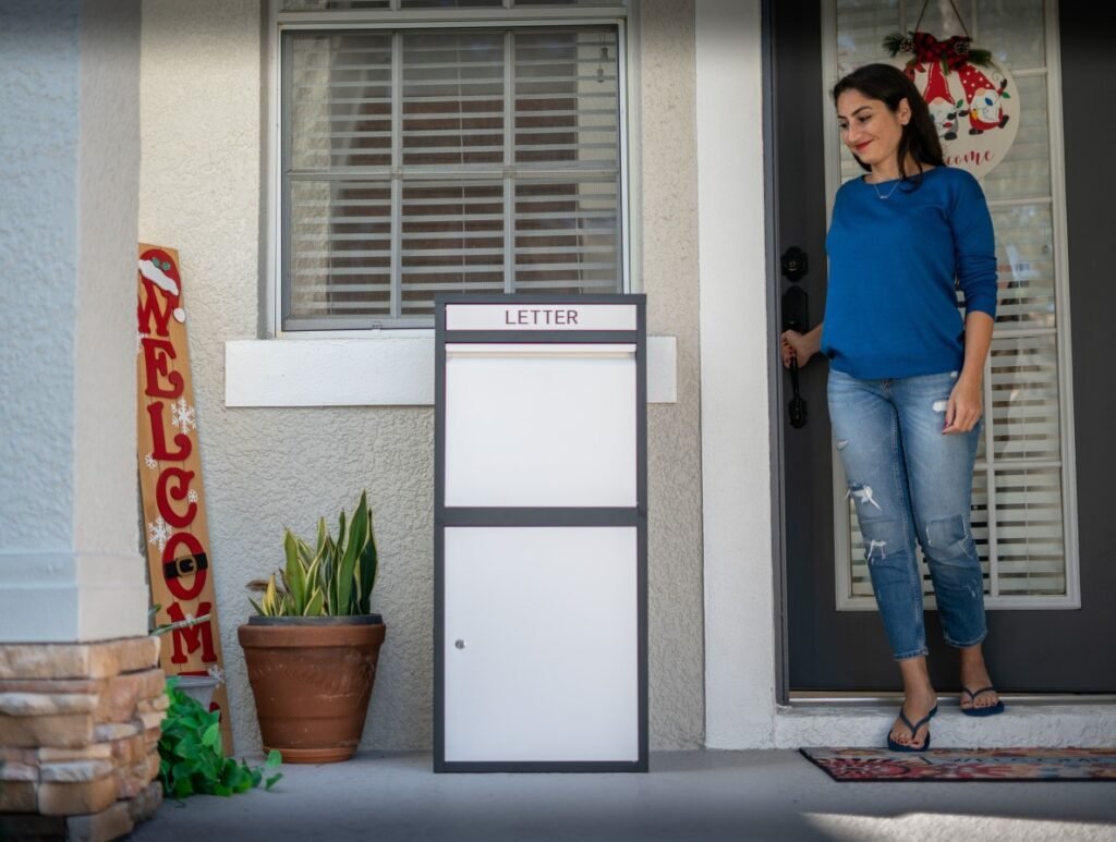 Una mujer elegante vestida con un suéter azul y jeans rotos se encuentra cerca de una caja de correo y paquete blanca y negra de Feliluke, exudando una sensación de anticipación. Los alrededores están adornados con diversas decoraciones vecinales.